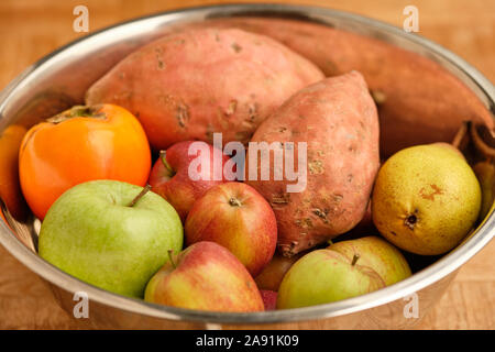 Sfondo colorato con sani frutti e verdure come le mele, kaki e patate dolci menzogne vicino insieme in un stagno argento ciotola. Foto Stock