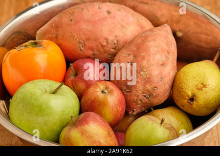 Sfondo colorato con sani frutti e verdure come le mele, kaki e patate dolci menzogne vicino insieme in un stagno argento ciotola. Foto Stock