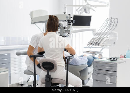 Vista posteriore di due dentisti dando il trattamento al paziente Foto Stock