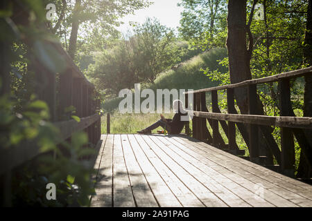 Donna seduta sul ponte di legno Foto Stock