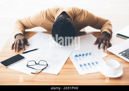 Sottolineato afro imprenditore con la testa in giù sul tavolo Foto Stock