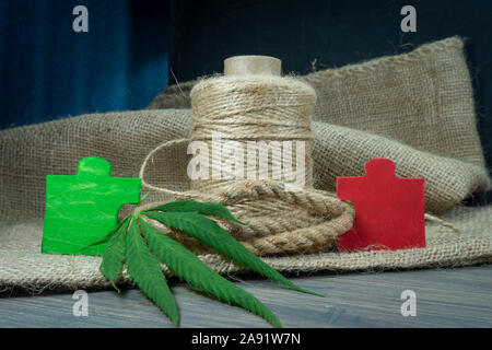 Tipi concettuale di prodotti a base di cannabis Concetto di immagine con una foglia di cannabis, rosso e verde puzzle in legno i pezzi del puzzle e naturali in fibra di canapa corda Foto Stock