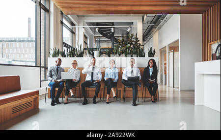 Gruppo sorridente di diversi imprenditori che lavorano insieme mentre è seduto in una fila l'area della reception di un ufficio moderno Foto Stock