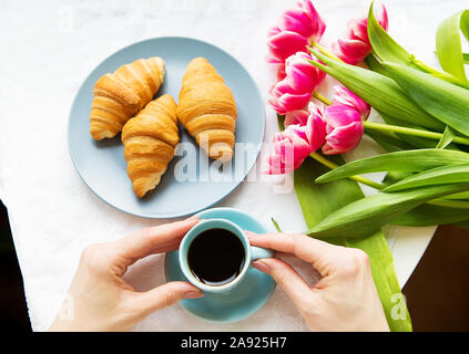 Ragazza con croissant e caffè, un bouquet di tulipani rosa, mattina felice. Foto Stock