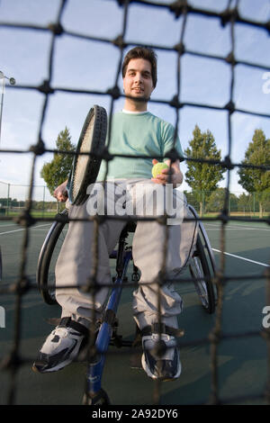 Ritratto di un giovane seduto su una sedia a rotelle e che gioca a tennis. Foto Stock