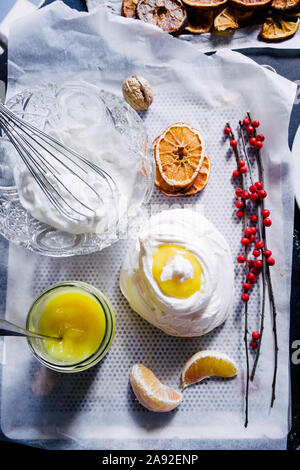 Nido di meringa al limone cagliata, con secchi fettine di arancia su uno sfondo nero, vista dall'alto, flatlay Foto Stock