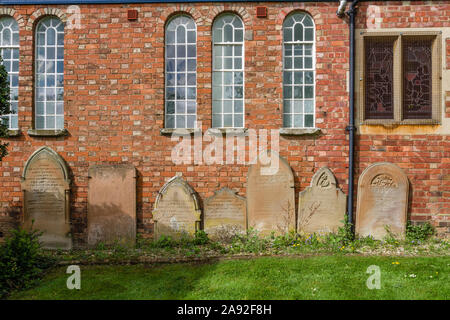 Vecchie lapidi schierati contro la parte esterna del Battista Cappella nel villaggio di Earls Barton, Northamptonshire, Regno Unito Foto Stock