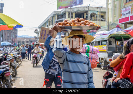 Giovane uomo che porta il cibo sulla testa nella strada trafficata; Lashio, Shan state, Myanmar Foto Stock