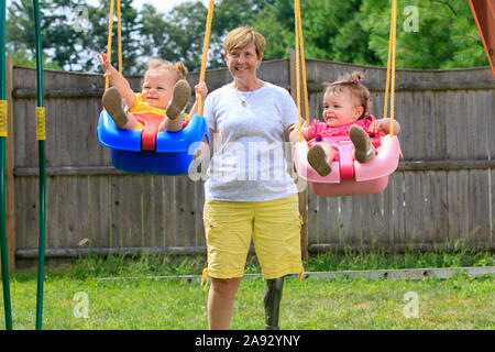 Nonna con una gamba protesica che gioca su un set swing con i suoi nipoti Foto Stock