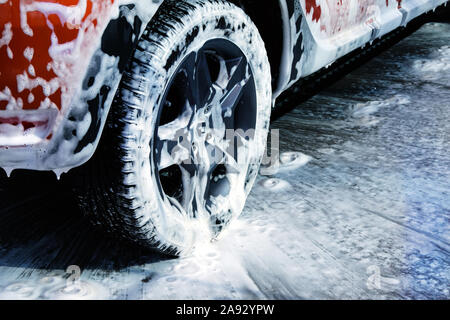 Ruota auto vicino. Auto è la pulizia con schiuma di sapone al self service car wash. Schiuma bianca su auto. Foto Stock