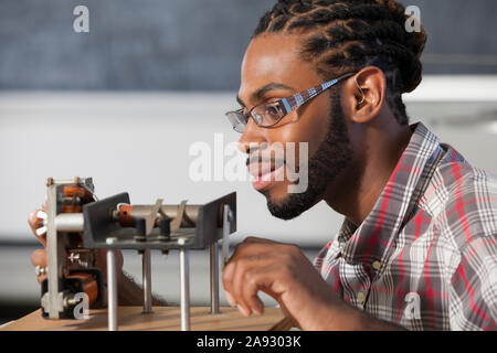 Studente che ha avuto meningite spinale con un apparecchio acustico, lavorando ad un esperimento di elettromagnetismo in laboratorio Foto Stock