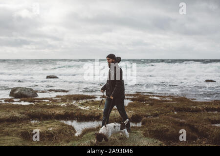 Uomo che cammina cane lungo la costa Foto Stock