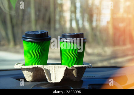 Verde di due bicchieri di carta con tè o caffè per un paio in auto sulla soleggiata sfondo sfocato. Takeaway, social media. La colazione del mattino in auto. Foto Stock