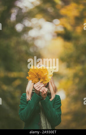 Donna che copre il volto con la caduta di foglie mentre gode in autunno e trascorrere il tempo nel parco. Foto Stock