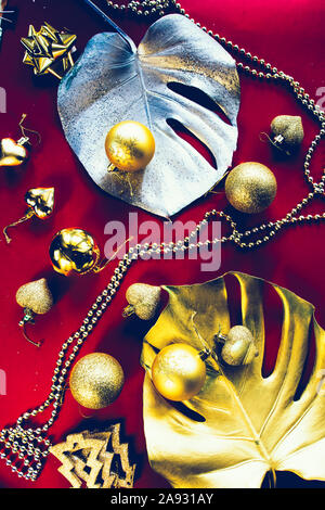 Esotiche della festa di natale, due giganti di monstera foglie dipinte di oro e di argento con goldne dcoration natale su uno sfondo rosso, vista dall'alto, chris Foto Stock