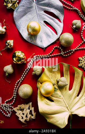 Esotiche della festa di natale, due giganti di monstera foglie dipinte di oro e di argento con goldne dcoration natale su uno sfondo rosso, vista dall'alto, chris Foto Stock