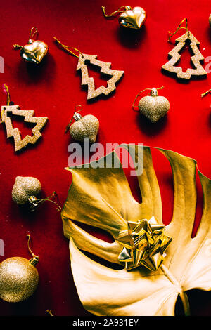 Esotiche della festa di natale, due giganti di monstera foglie dipinte di oro e di argento con goldne dcoration natale su uno sfondo rosso, vista dall'alto, chris Foto Stock