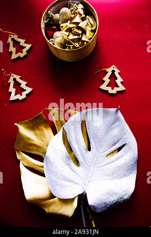 Esotiche della festa di natale, due giganti di monstera foglie dipinte di oro e di argento con goldne dcoration natale su uno sfondo rosso, vista dall'alto, chris Foto Stock