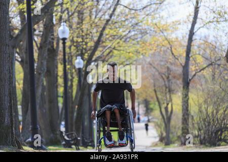 Uomo su una sedia a rotelle che ha avuto meningite spinale che passa attraverso un parco Foto Stock
