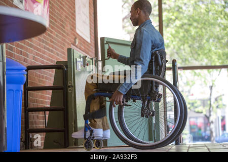 Uomo che ha avuto meningite spinale in una sedia a rotelle usando un ascensore invece di scale Foto Stock