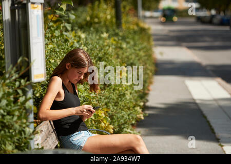 Donna seduta sul bus stop Foto Stock