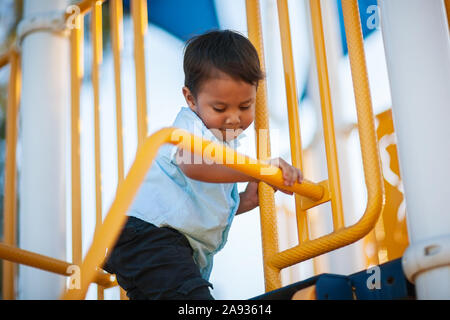 Un ispanico bambino maschio utilizzando le mani e i piedi per carefuly equilibrio come egli si arrampica una giungla palestra parco giochi. Foto Stock