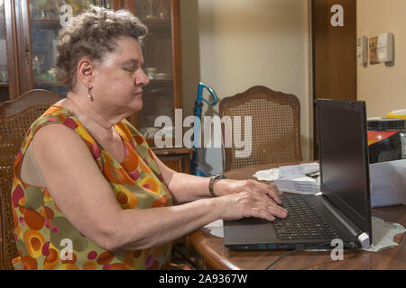 Donna anziana cieca che usa il suo laptop a casa Foto Stock