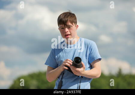 Giovane uomo con sindrome di Down che tiene una macchina fotografica Foto Stock
