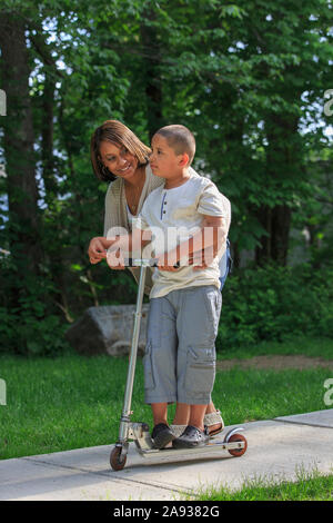 Ragazzo ispanico con autismo che gioca su uno scooter push con sua madre Foto Stock