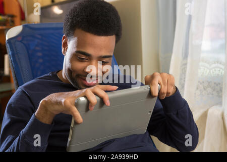 Felice uomo afroamericano con paralisi cerebrale utilizzando la sua tavoletta a casa Foto Stock