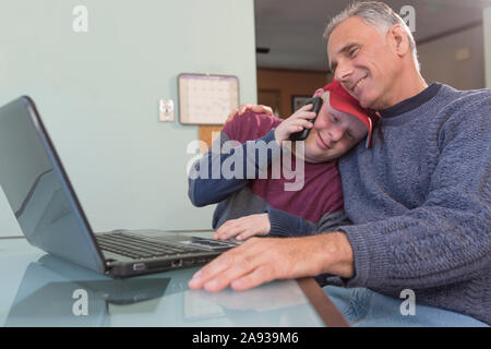 Giovane uomo con la sindrome di Down abbracciando il padre con la spina dorsale Lesioni al cavo a casa Foto Stock
