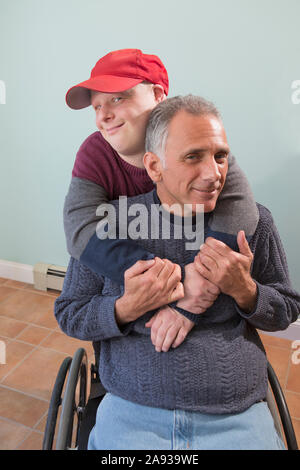 Ritratto di felice giovane con la sindrome di Down e la sua padre in sedia a rotelle con lesione del midollo spinale a casa Foto Stock