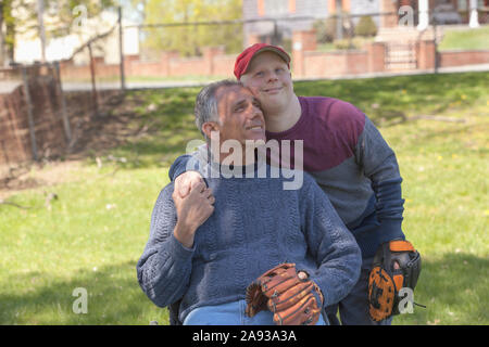Padre con lesione del midollo spinale e suo figlio con giù Sindrome che sta per giocare a baseball nel parco Foto Stock