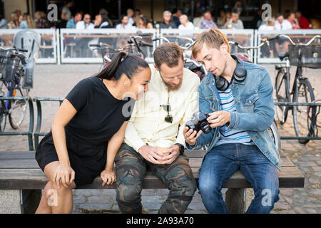 Gli amici su banco guardando lo schermo della fotocamera Foto Stock