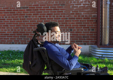 Felice uomo afroamericano con paralisi cerebrale usando il suo potere sedia a rotelle all'esterno Foto Stock