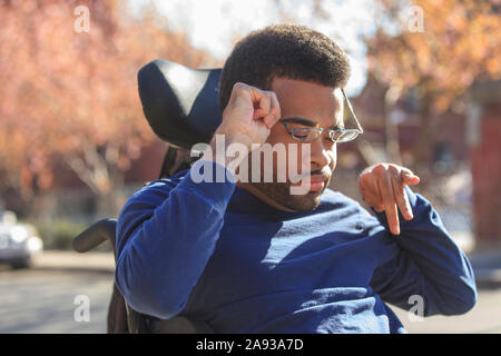 Uomo afroamericano con paralisi cerebrale che mette sugli occhiali la sua sedia a rotelle di potere fuori Foto Stock