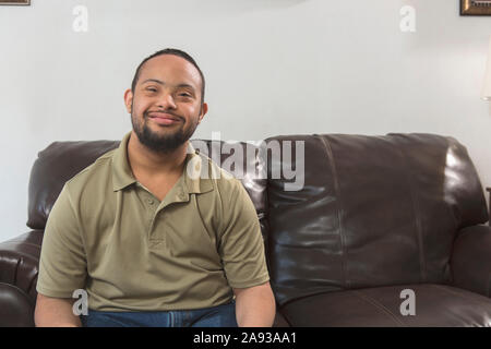 Ritratto dell'uomo afro-americano felice con la sindrome di Down seduta sul divano a casa Foto Stock