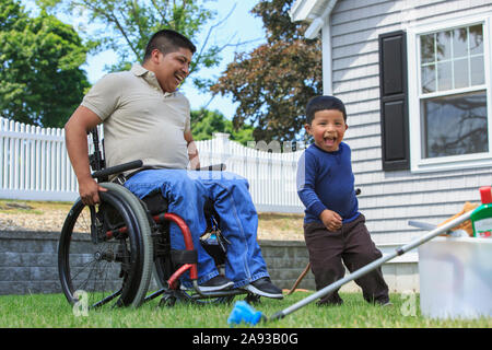 Uomo ispanico con lesione del midollo spinale in sedia a rotelle con la sua figlio che si prepara a lavare un'auto Foto Stock