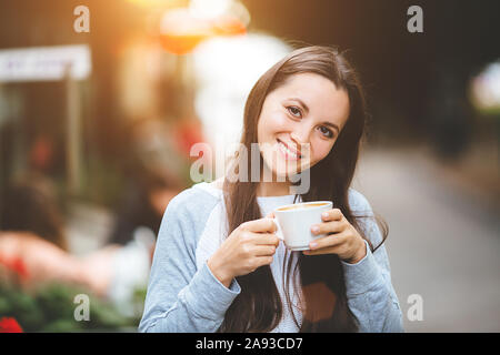 Outdoor ritratto di una giovane ragazza , lavora come libero professionista in un cafe, bere una deliziosa tazza di caffè caldo, dal testo invia mail carica le foto instagram freelancer bere il cappuccino. Foto Stock