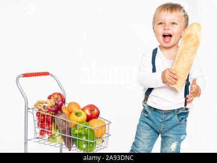 Allegro little boy in abiti casual in piedi in studio con cibo sano cestello. Shopping, sconto, vendita concetto isolato su sfondo bianco Foto Stock