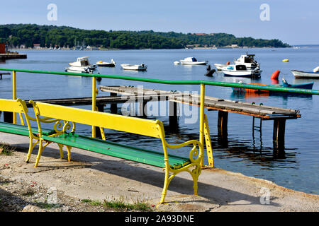 Svuotare il giallo e il verde panchina affacciato sul porticciolo e sul mare con barche di Pola, Croazia Foto Stock