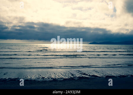 Drammatica cielo nuvoloso con lieve sunburst guardando fuori di Kapiti Island e oltre lo stretto di Cook da Raumati Beach, Wellington, Nuova Zelanda Foto Stock