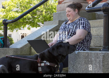 Donna con compromissione visiva seduta con il suo cane di servizio e. utilizzando un computer Foto Stock