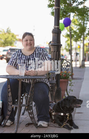 Donna con disabilità visiva seduta in un bar con lei cane di manutenzione Foto Stock