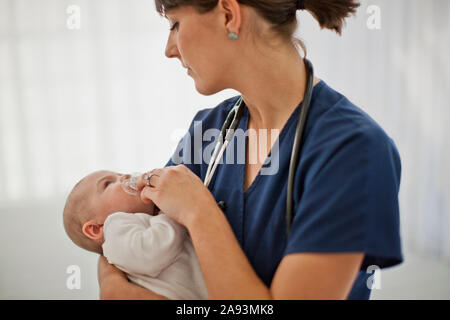 Bambino ragazzo guardando in su l'infermiera giovane che tiene delicatamente lui Foto Stock