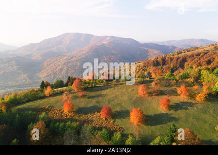 Autunno pittoresco prato con casa in legno rosso e faggi in montagna Foto Stock