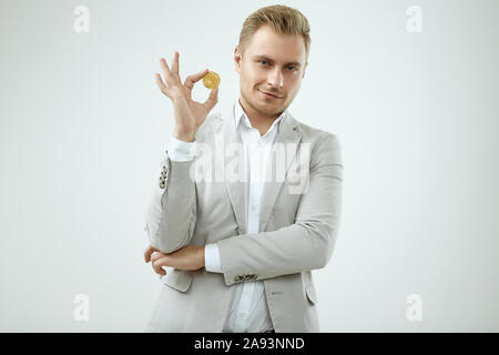 Ritratto di una bella bionda modello da uomo in modo completo grigio contiene un Bitcoin isolati su sfondo bianco in studio Foto Stock