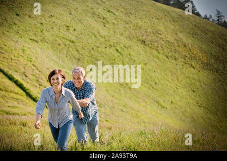 Sorridente Coppia matura camminare insieme attraverso un campo erboso nel paese. Foto Stock