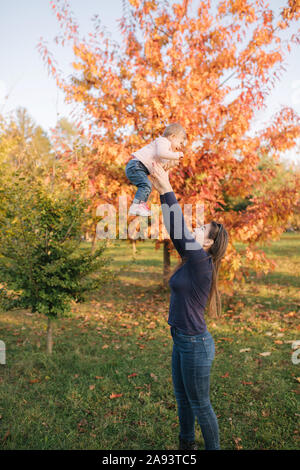 Vista laterale di felice giovane madre holding Baby girl nelle sue mani e guardando a Lei con amore. Autunno photosession Foto Stock