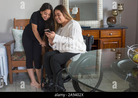 Donna che ha lesione del midollo spinale che legge un testo con sua sorella Foto Stock